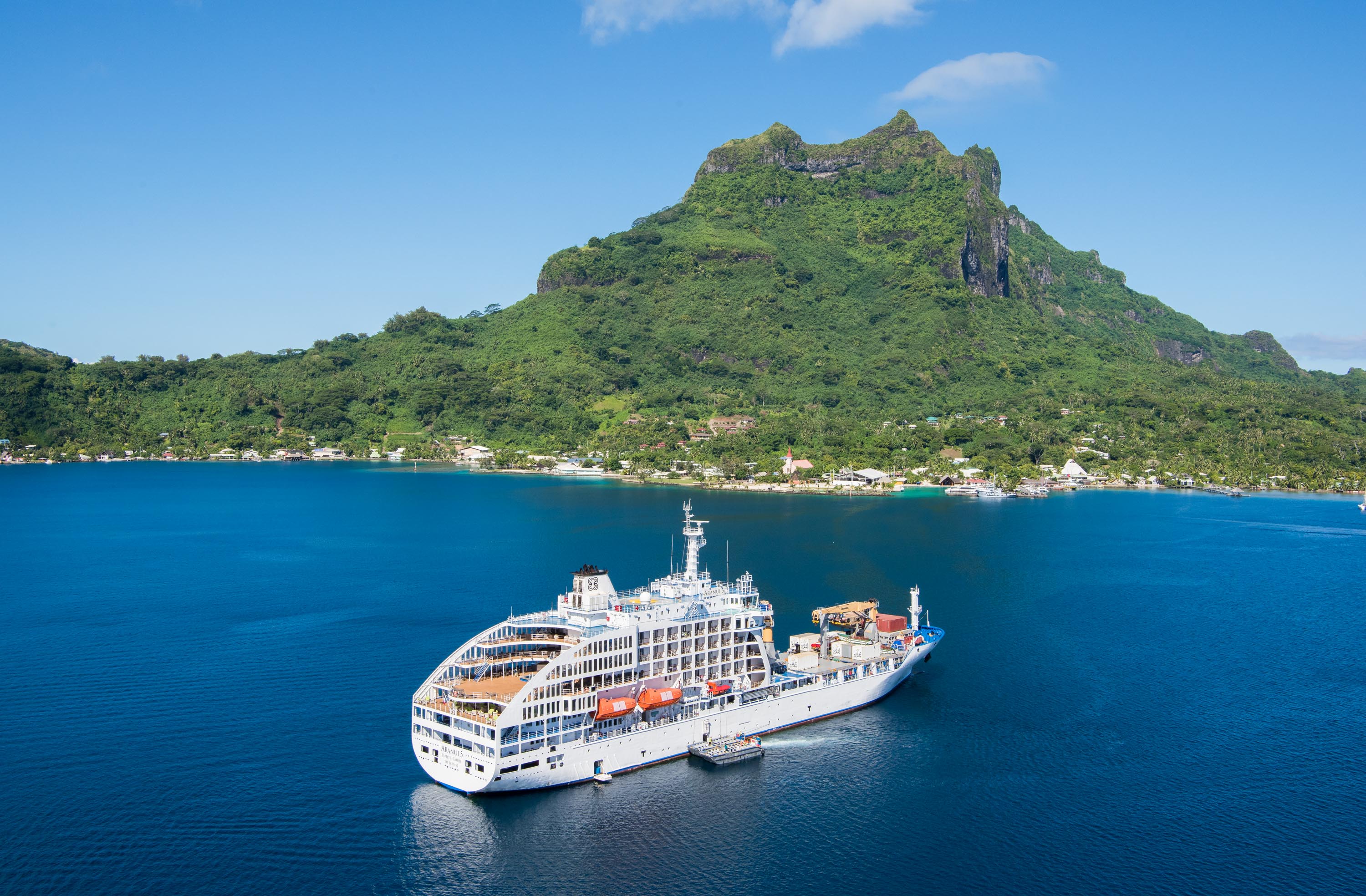 A luxurious Aranui cruise ship sailing through clear blue waters near a lush tropical island.
